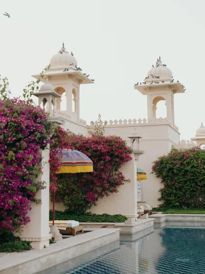 The stunning architecture and poolside of The Oberoi Udaivilas, blooming with bougainvillea, setting the scene for a luxurious destination wedding.