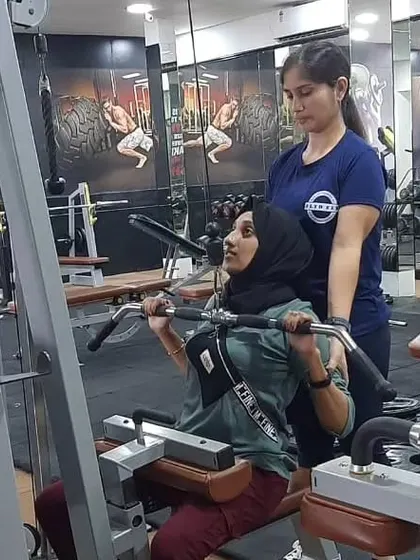 One-on-one guidance is a key part of our practical training. Here, an instructor helps a student with her form on the lat pulldown machine, ensuring she activates the correct muscles for an effective and safe workout.