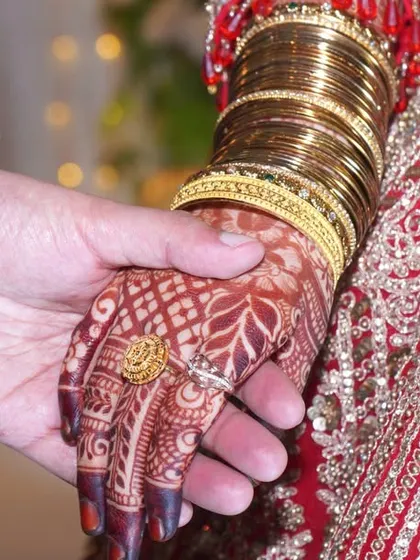 A close-up of the couple holding hands, showing the bride's intricate henna and wedding ring.