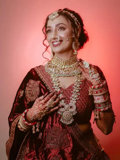 A stunning bridal portrait with dramatic lighting, highlighting the rich velvet of her lehenga and her radiant smile.