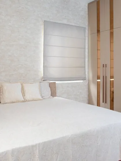 A wider view of the bedroom, showing how the neutral wardrobe with metallic accents complements the soft, textured wallpaper and clean white bedding to create a calm and elegant space.