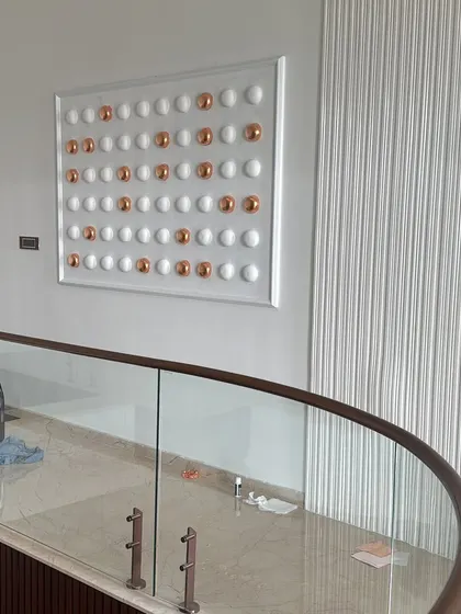 This minimalist piece features a symmetrical grid of white and copper-foiled spheres. It's a modern and classy relief sculpture that adds a touch of sophistication to this staircase landing.