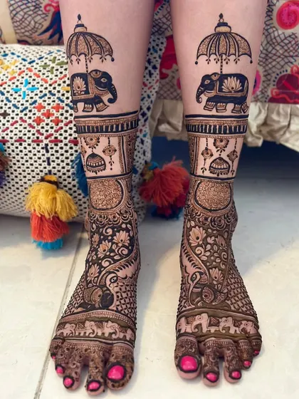 A whimsical and royal design for bridal legs. It features elephants holding umbrellas, along with jhumkis and peacocks, creating a full and festive look.