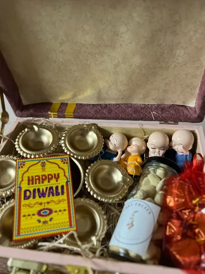 Another view of the pink velvet-lined box, showing the arrangement of diyas, monk figurines, and a jar of sweets.