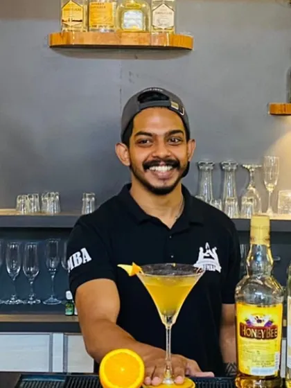 A smiling bartender presents his orange-garnished cocktail, ready to be served.