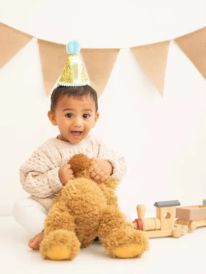 It's not a party without a hat! This little one is ready to celebrate his first birthday, teddy bear in tow.