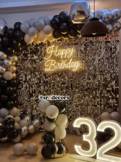 A stylish 32nd birthday decoration featuring a silver shimmer wall, a black and silver balloon frame, and a glowing neon sign.
