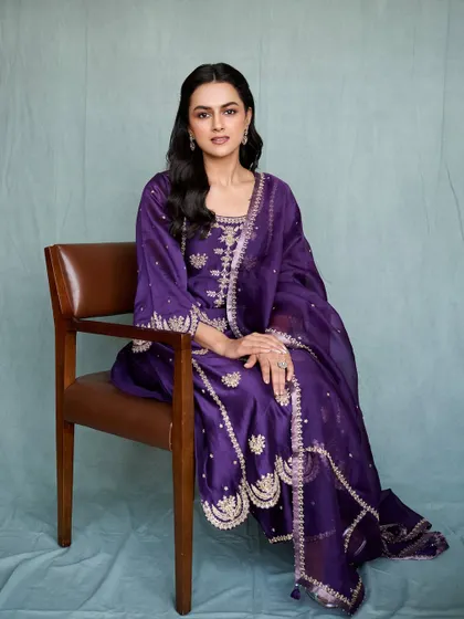 A full, seated portrait of Shraddha in the purple suit. The styling is classic, letting the outfit and her personality shine.