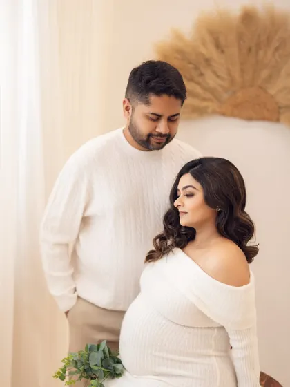 Soft, cozy, and full of warmth. This couple, dressed in coordinating white knit sweaters, shares a quiet moment in a boho-inspired studio setup, perfect for a winter or fall themed maternity photoshoot.