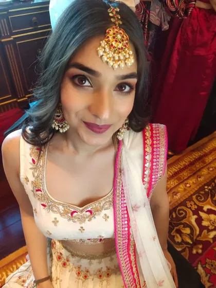 A classic festive look featuring a maang tikka. The makeup includes soft smokey eyes and a bold berry lip, perfectly coordinated with her white and pink embroidered lehenga.