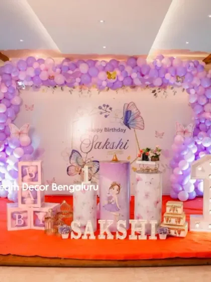 A full view of Sakshi's butterfly-themed first birthday. The purple balloon arch and themed backdrop create a beautiful and cohesive look on the stage.