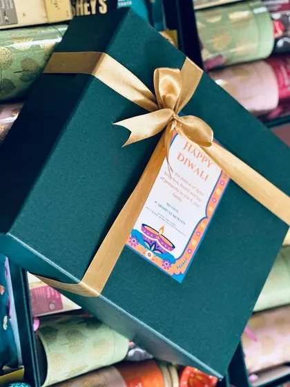 A custom Diwali gift hamper created for a member of the South Western Railways, featuring a deep green box, gold ribbon, and a personalized "Happy Diwali" tag.
