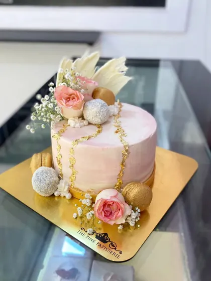 A delicate and pretty pink cake with a watercolor finish. It's adorned with gold chains, fresh roses, baby's breath, and sparkling white and gold spheres.
