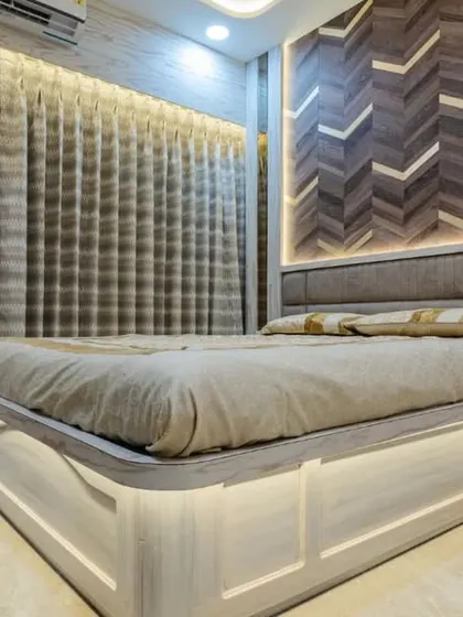 This bedroom in Mahad features a striking chevron-patterned wood headboard wall with integrated lighting. The floating bed design enhances the modern aesthetic and makes the room feel more spacious.