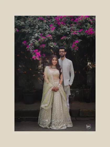 A full-length portrait showcasing the couple's beautifully coordinated pastel outfits for their Mehendi ceremony. The classic pose against a floral backdrop is both elegant and timeless.