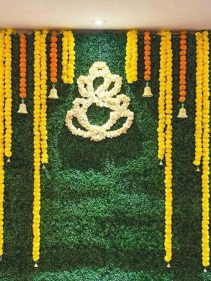 A popular choice for home festivals, this backdrop uses a green wall, marigold garlands, and a floral Ganesha outline for a traditional yet clean look.