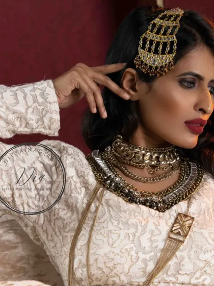 This profile shot highlights the unique hair accessory and layered necklaces from a high-fashion shoot. The makeup is kept strong and defined to balance the bold styling of the overall look.