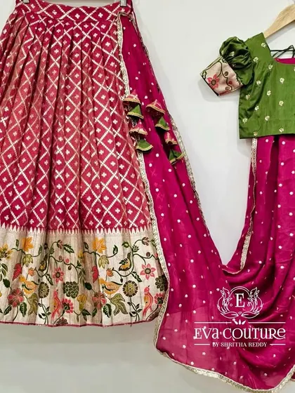 A beautiful Banarasi lehenga with a floral border. The magenta skirt has a diamond pattern weave, paired with a simple green blouse with printed puff sleeves.
