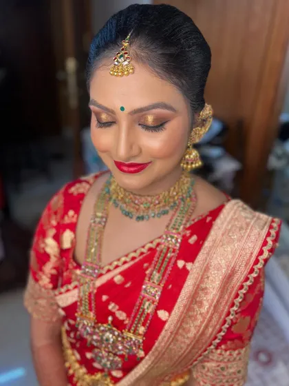A beautiful 'buttabomma' look. The makeup features classic gold eyes and a bold red lip, a perfect combination for her traditional South Indian bridal attire.