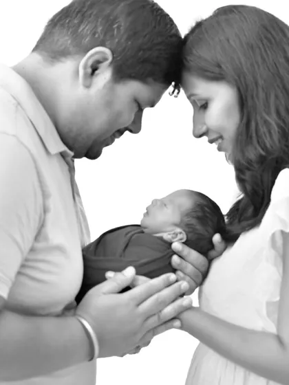 An intimate black and white portrait of new parents, their foreheads touching as they lovingly hold their newborn baby together, symbolizing their complete world.