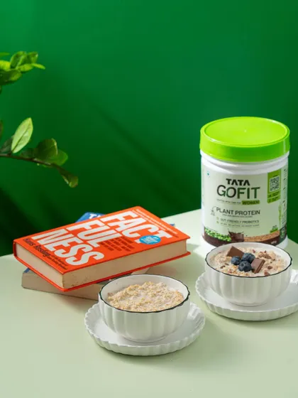 A lifestyle product shot for Tata GoFit, showing the protein powder as part of a healthy morning routine with oatmeal and books.