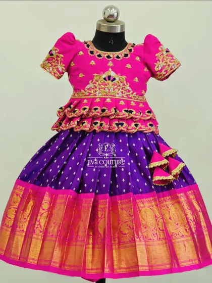 A vibrant pink and purple Pattu Pavadai. The blouse has a tiered peplum design and is detailed with rich gold embroidery, matching the wide zari border on the skirt.