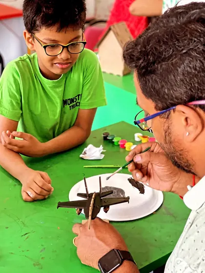 An instructor provides one-on-one guidance, showing a student a painting technique for his model airplane.