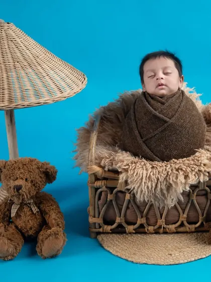 A cozy setup with a teddy bear and a wicker lamp. The baby is wrapped snugly in a basket, creating a warm and inviting scene.