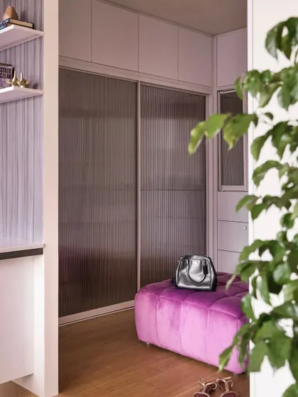 Another view of the walk-in closet, showing the purple pouffe and the elegant fluted glass sliding doors of the wardrobe.