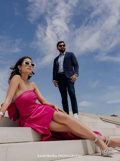A low-angle shot of the couple on the steps of the modern building in Baku, set against a dramatic blue sky.