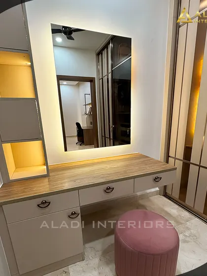 A sleek vanity table with a large backlit mirror, providing perfect lighting for getting ready. The design includes drawers for storage and is paired with a comfortable pink stool.