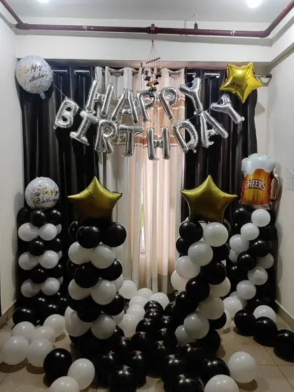 A black and white themed room decoration with balloon pillars and "Happy Birthday" foil letters.