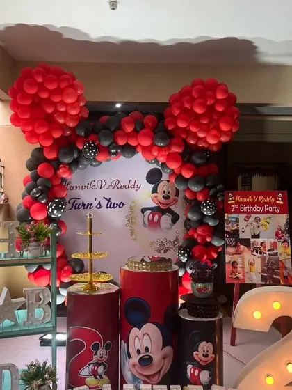 A Mickey Mouse theme for a second birthday, featuring large red balloon ears on the arch and character-printed pedestals.