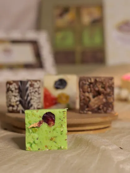A close-up of our Pista Kunafa fudge, a unique creation with a vibrant green color and a delicate rose petal garnish. It's a dense, rich, and flavorful treat.