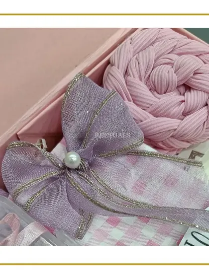 A detail shot of the gift wrapping for the baby set, featuring a lavender bow and a pink braided cloth.