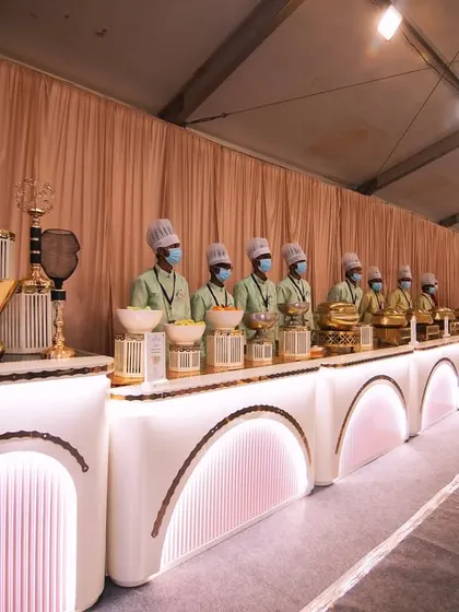 A long shot of the VIP buffet line at a grand wedding. The clean, white, and gold arched counters create a look of pure elegance and sophistication.