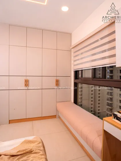 This floor-to-ceiling wardrobe in a light neutral tone includes a cozy window seat with built-in storage, making smart use of space.