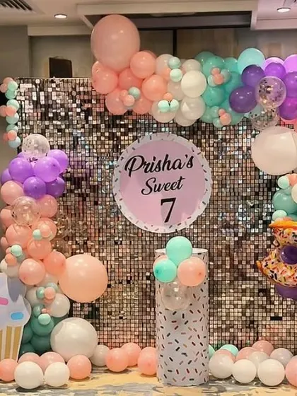 A "Sweet 7" party with a donut and cupcake theme, a sequin wall, and pastel-colored balloons.