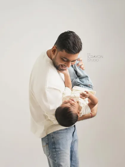 A father holds his toddler upside down, sharing a moment of pure, uninhibited laughter in the studio.