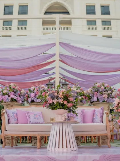 The main stage for the Bridgerton Mehendi, featuring a plush sofa, abundant florals, and a backdrop of soft, draped fabrics, creating a picture-perfect spot for the couple.