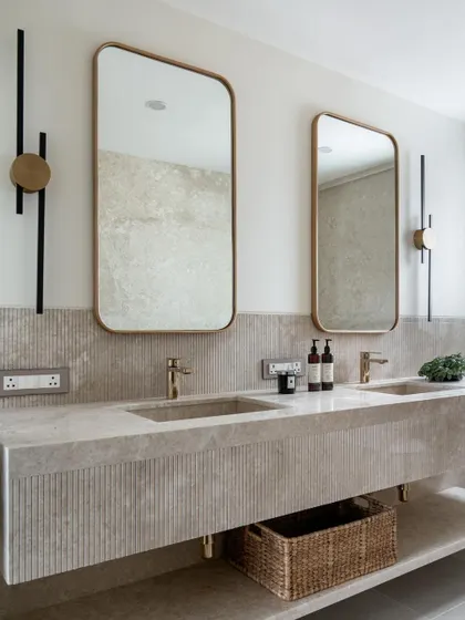 This luxurious master bathroom features a floating double vanity made of fluted stone. The large mirrors and modern sconces create a symmetrical and elegant space.