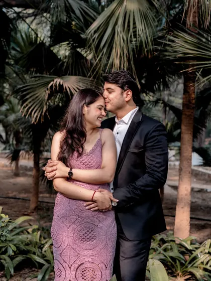 A tender forehead kiss surrounded by lush palm trees. The natural greenery provides a beautiful, intimate backdrop for this romantic gesture.