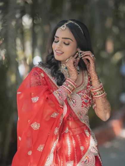 The final moments of getting ready are so special. This bride is adjusting her earrings, showcasing the beautiful harmony between her soft glam makeup, traditional red attire, and elegant jewellery.