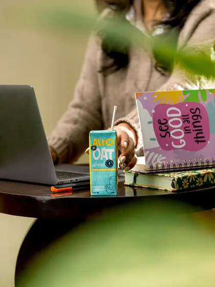 A relatable lifestyle scene showing Alt Co.'s oat milk carton on a desk next to a laptop. This places the product directly into the daily life of a student or professional as a convenient and healthy drink.