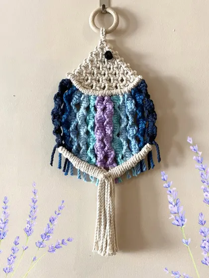 A single macrame fish in cool shades of blue and purple. The wooden ring makes it easy to hang anywhere you need a splash of color.