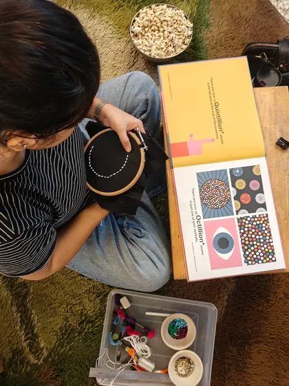 A parent works on an embroidery piece, drawing inspiration from a book. Each stitch in our community canopy represents a story and a hope for the children stepping out into the world from our school.