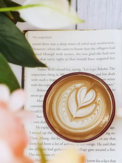A perfect cup of latte with beautiful art rests on an open book. This classic pairing evokes a sense of quiet contemplation and the simple pleasure of a coffee break.