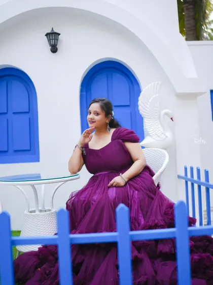 A beautiful solo portrait of the bride-to-be in a stunning purple gown, set against a Santorini-style white and blue backdrop.