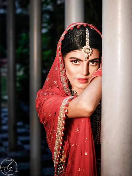 A striking bridal portrait where the bride peeks from behind a pillar. Her direct gaze and bold red lipstick create a powerful and confident image that is both modern and traditional.