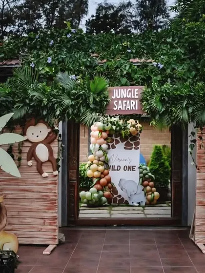 An immersive jungle safari entrance for a "Wild One" first birthday party. Guests are welcomed through a wooden gate adorned with animal cutouts and lush greenery.
